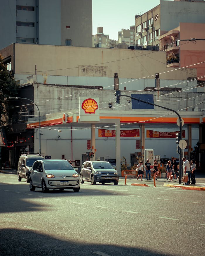 Street scene in Buenos Aires featuring cars passing a Shell gas station, with pedestrians and urban backdrop.