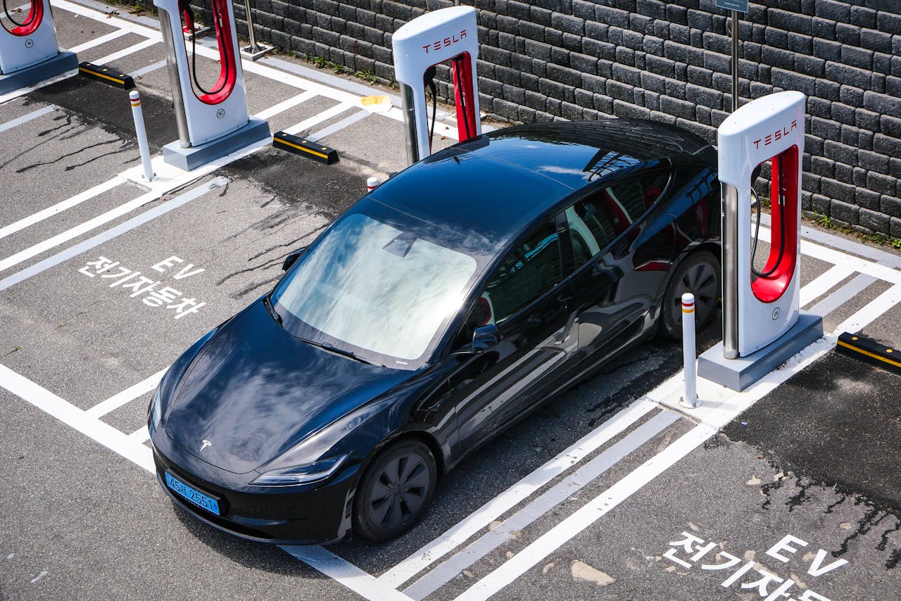 A black Tesla parked at a charging station in an urban setting.