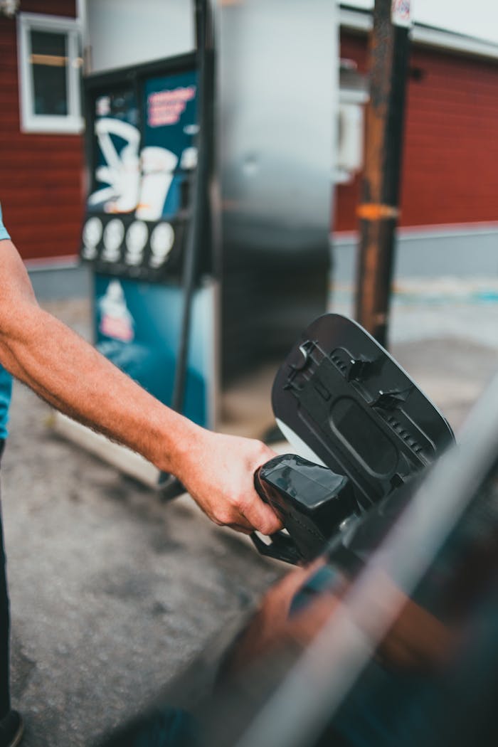 Close-up of a man refueling a car at a gas station, focusing on the gasoline pump.